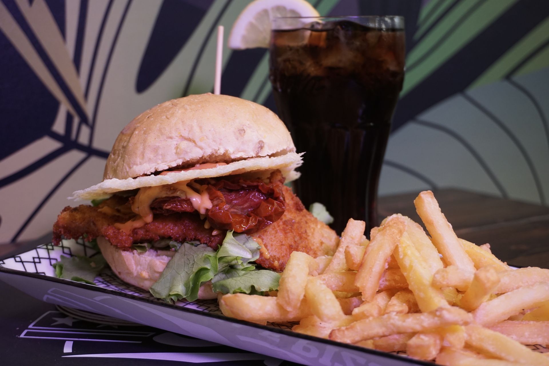Un hamburger e delle patatine fritte sono su un piatto accanto a un bicchiere di soda.