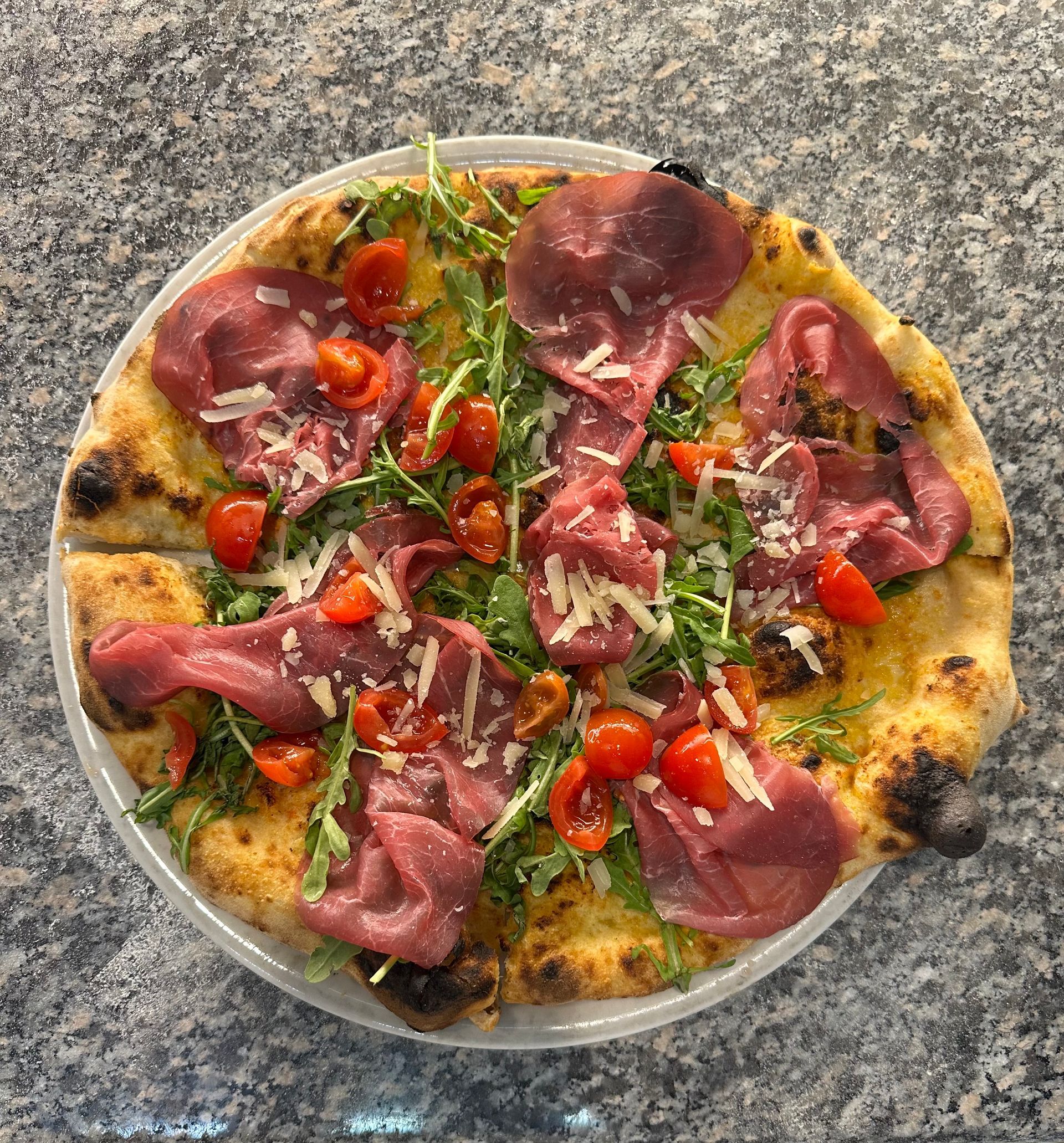 Una pizza con carne e pomodori su un piatto su un tavolo.