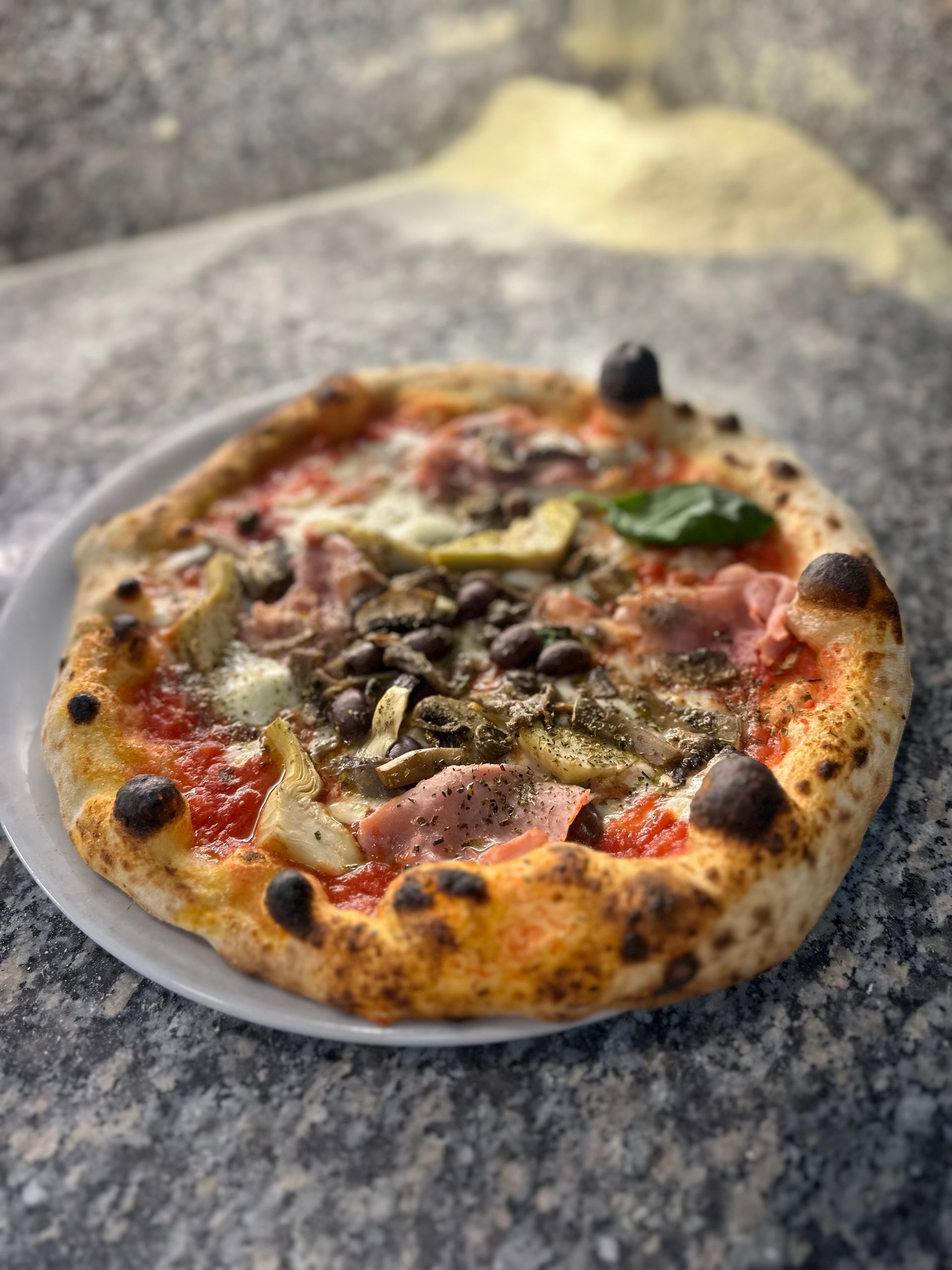 Una pizza è appoggiata su un piatto bianco su un tavolo.