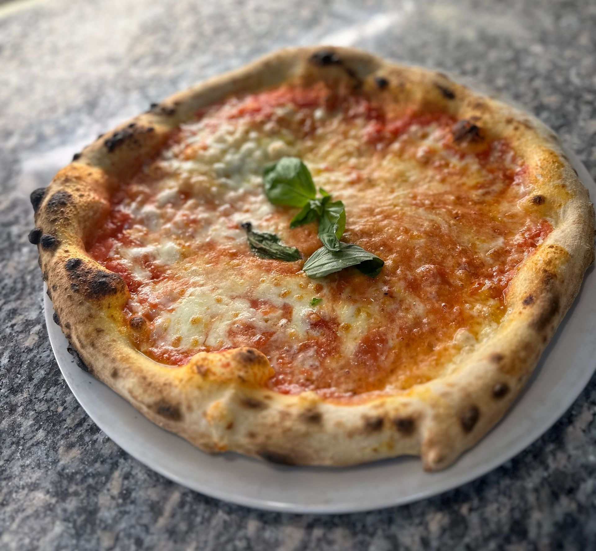 Una pizza è appoggiata su un piatto bianco su un tavolo.