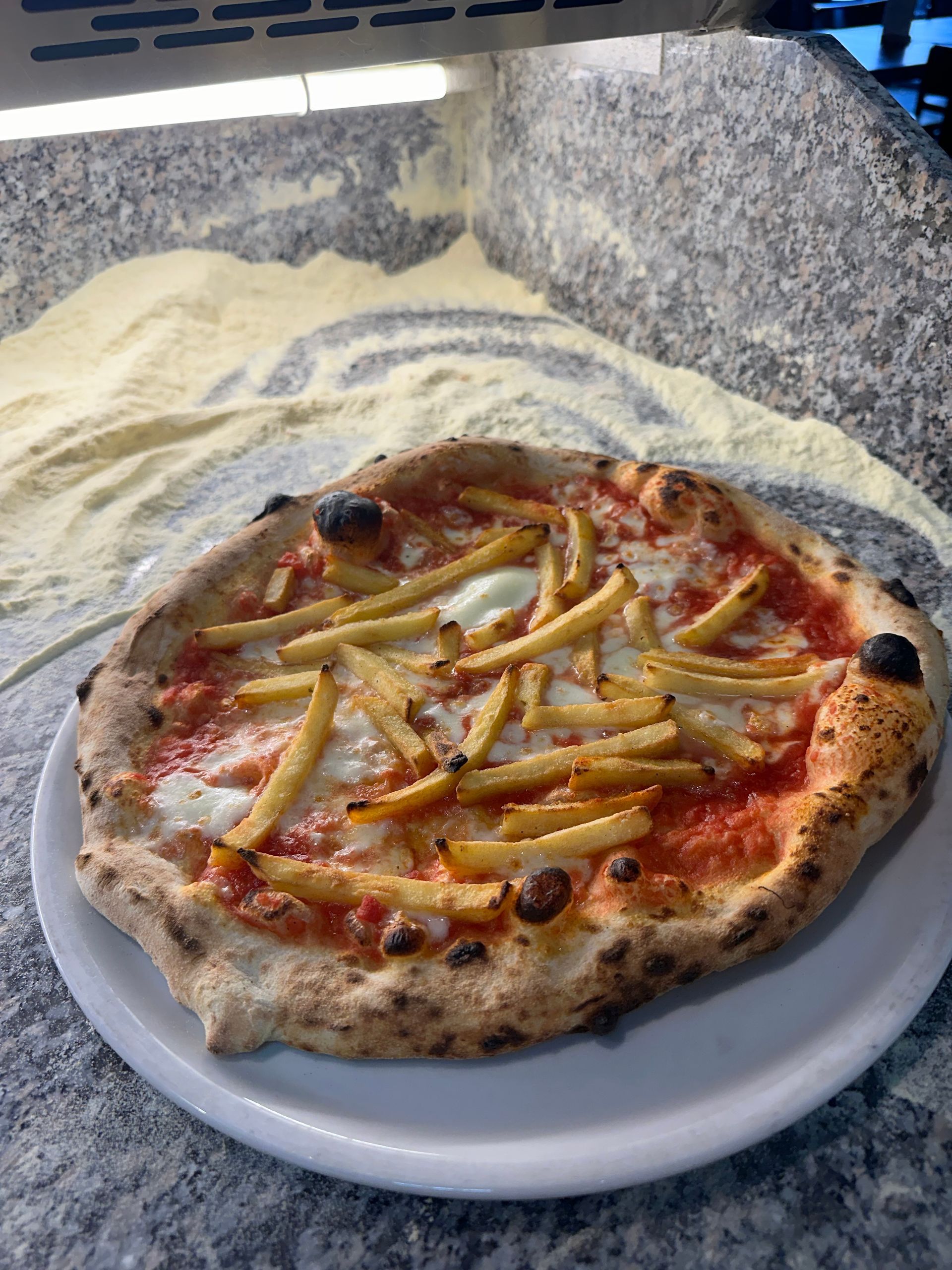 Una pizza con patatine fritte sopra è su un piatto bianco su un tavolo.