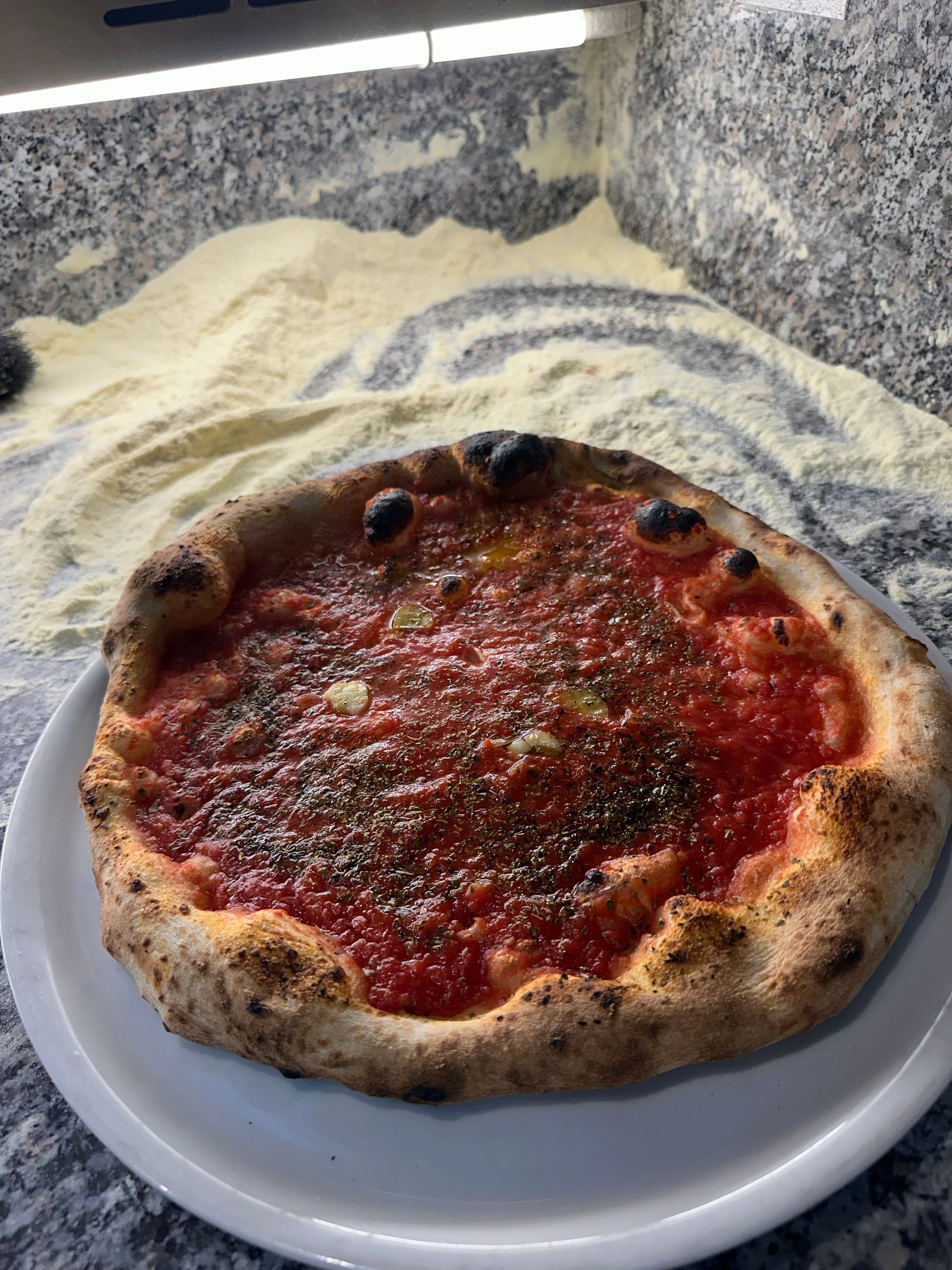Una pizza è appoggiata su un piatto bianco sul bancone.