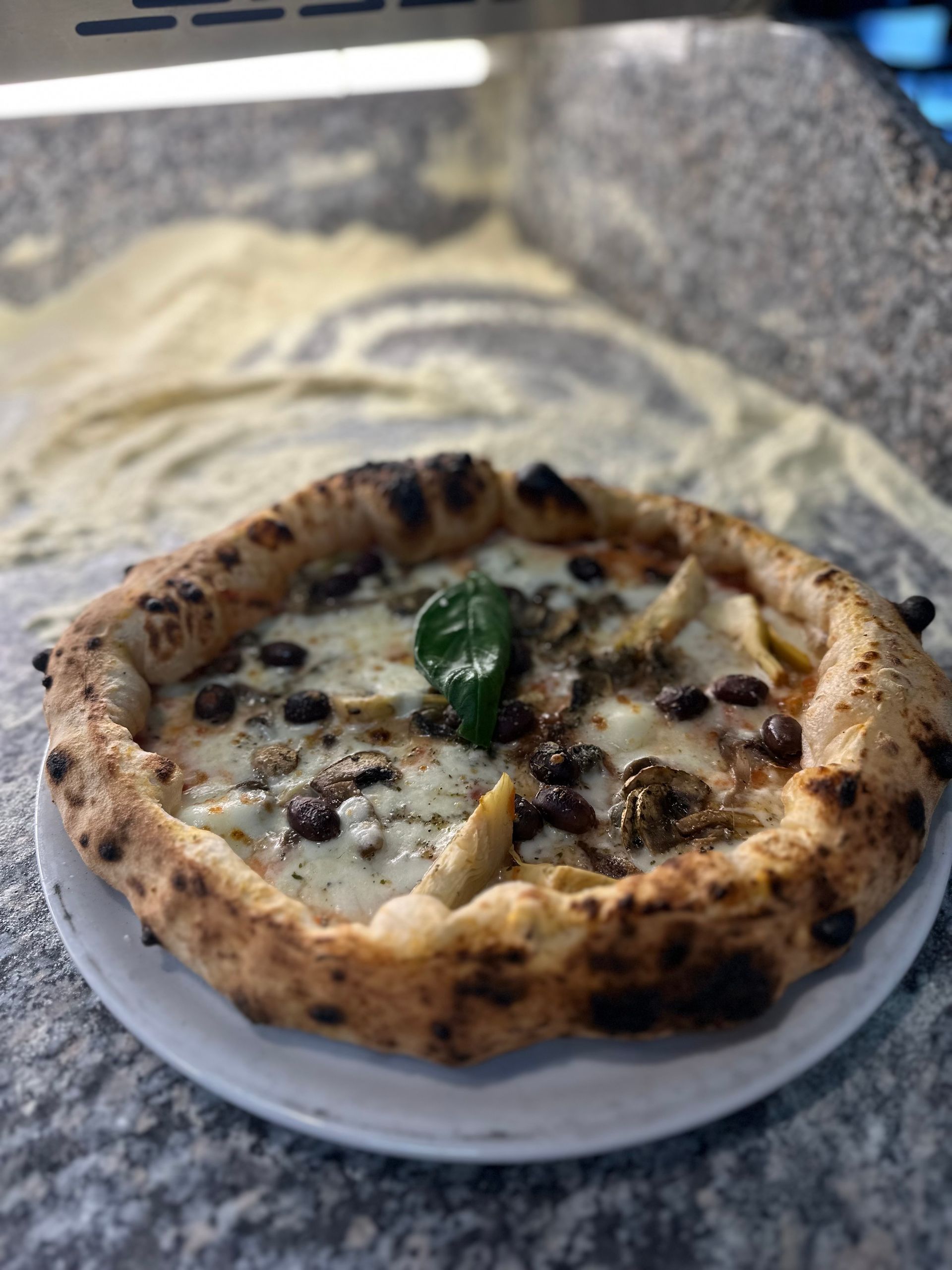 Una pizza è appoggiata su un piatto bianco sul bancone.