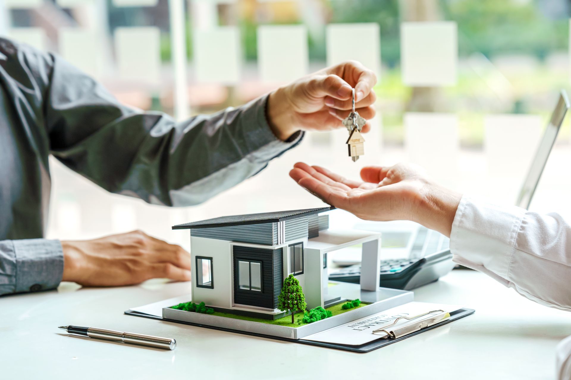A man is giving a key to another person in front of a model house.