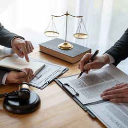 Two men are sitting at a table with a judge 's gavel and scales of justice.