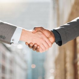 Two people are shaking hands in front of a building.