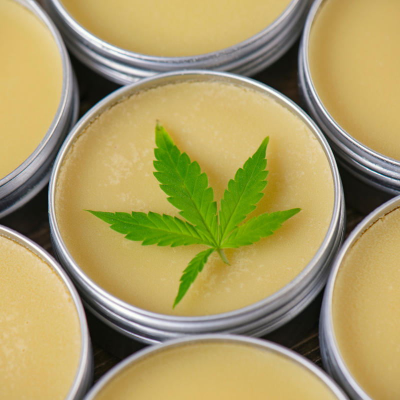 Topical balm infused with cannabis with a cannabis leaf laid on top