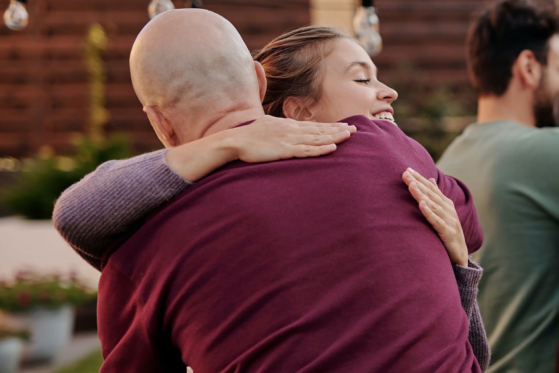 a woman in a purple shirt is hugging a bald man