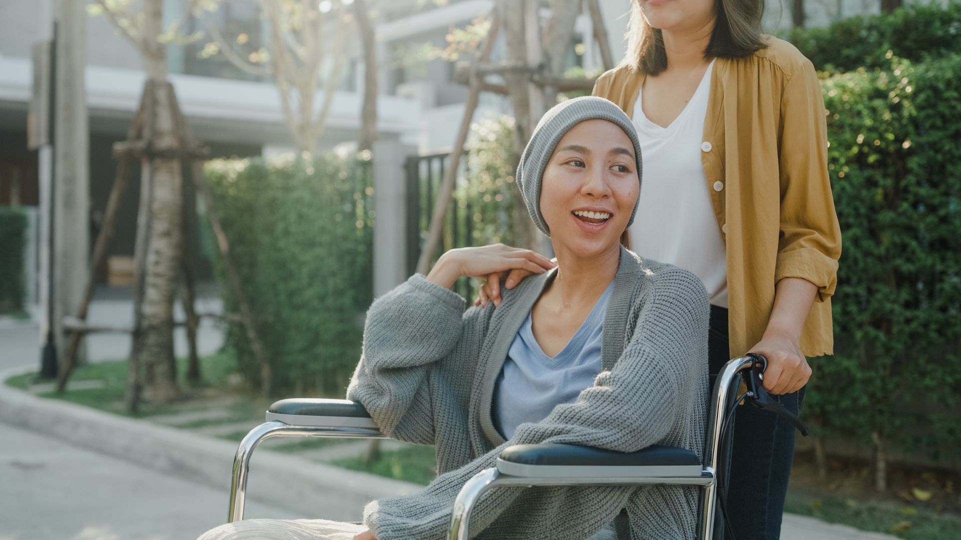 A young woman in a wheelchair holds the hand of her friend who is standing behind her