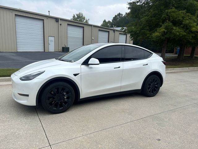 A white tesla model y is parked on the side of the road in front of a building.