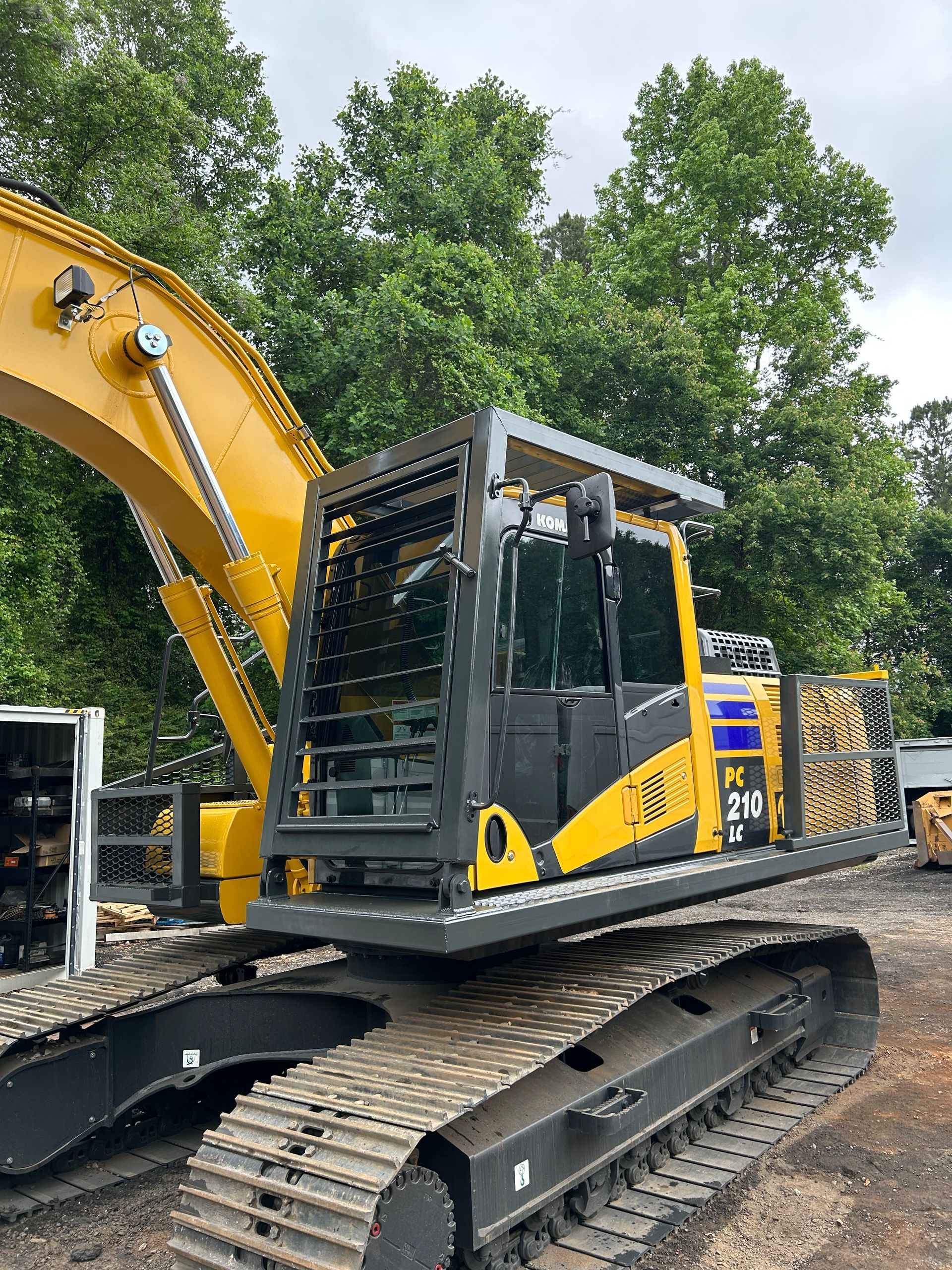 A yellow and black excavator is parked in front of trees.