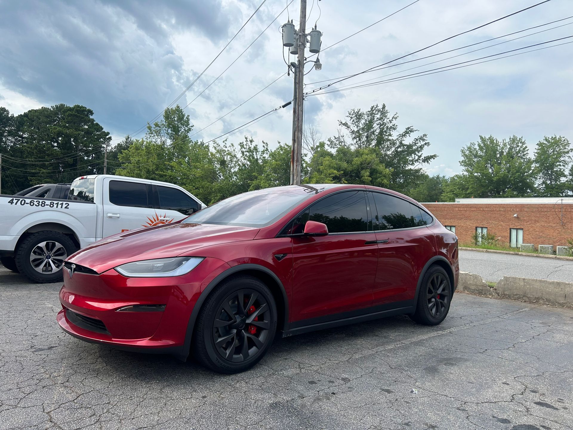 A red tesla model x is parked in a parking lot next to a white truck.