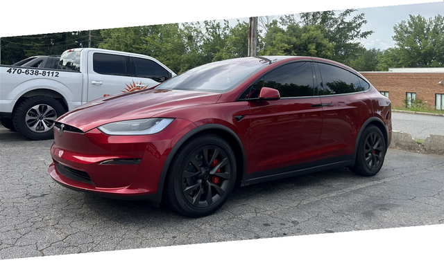 A red tesla model x is parked in a parking lot next to a white truck.