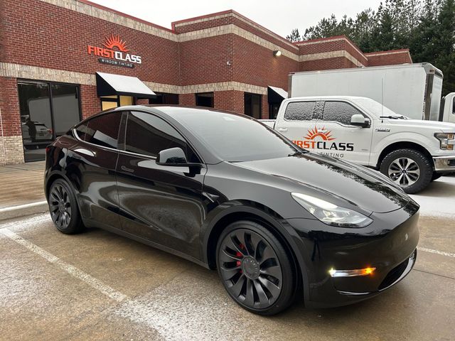 A black tesla model y is parked in front of a brick building.