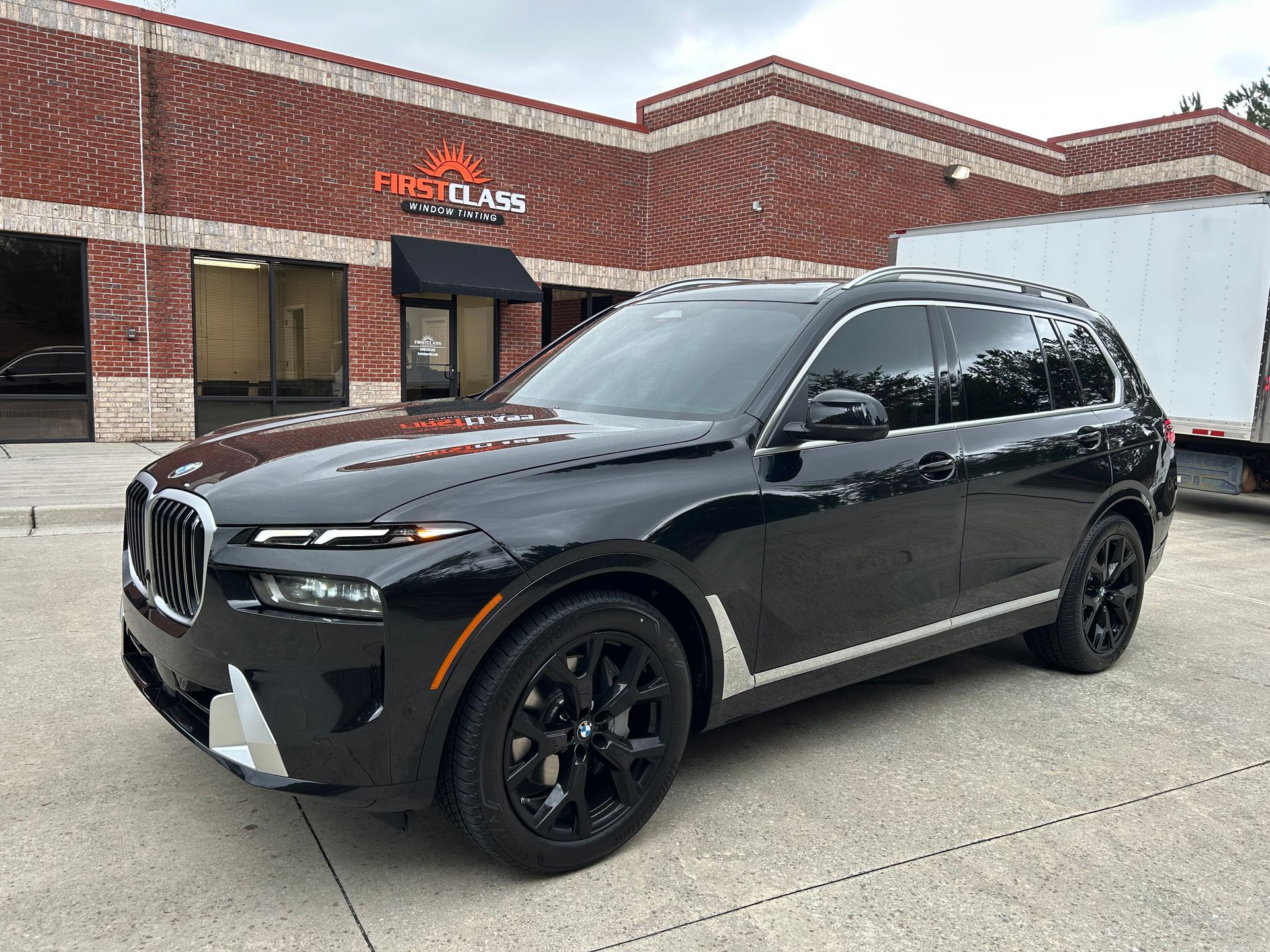 A black bmw x7 is parked in front of a brick building.
