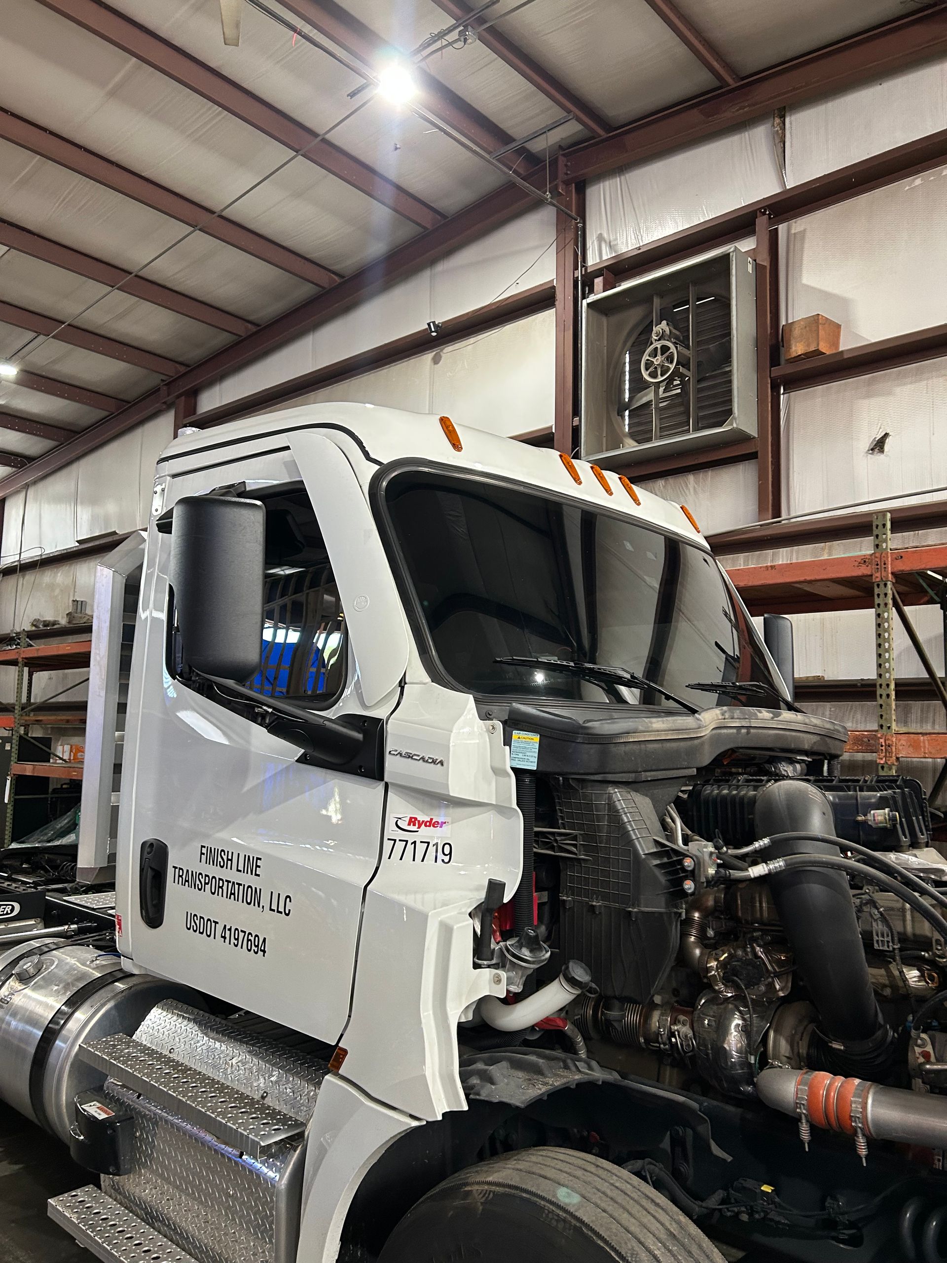 A semi truck is sitting in a garage with the hood up.