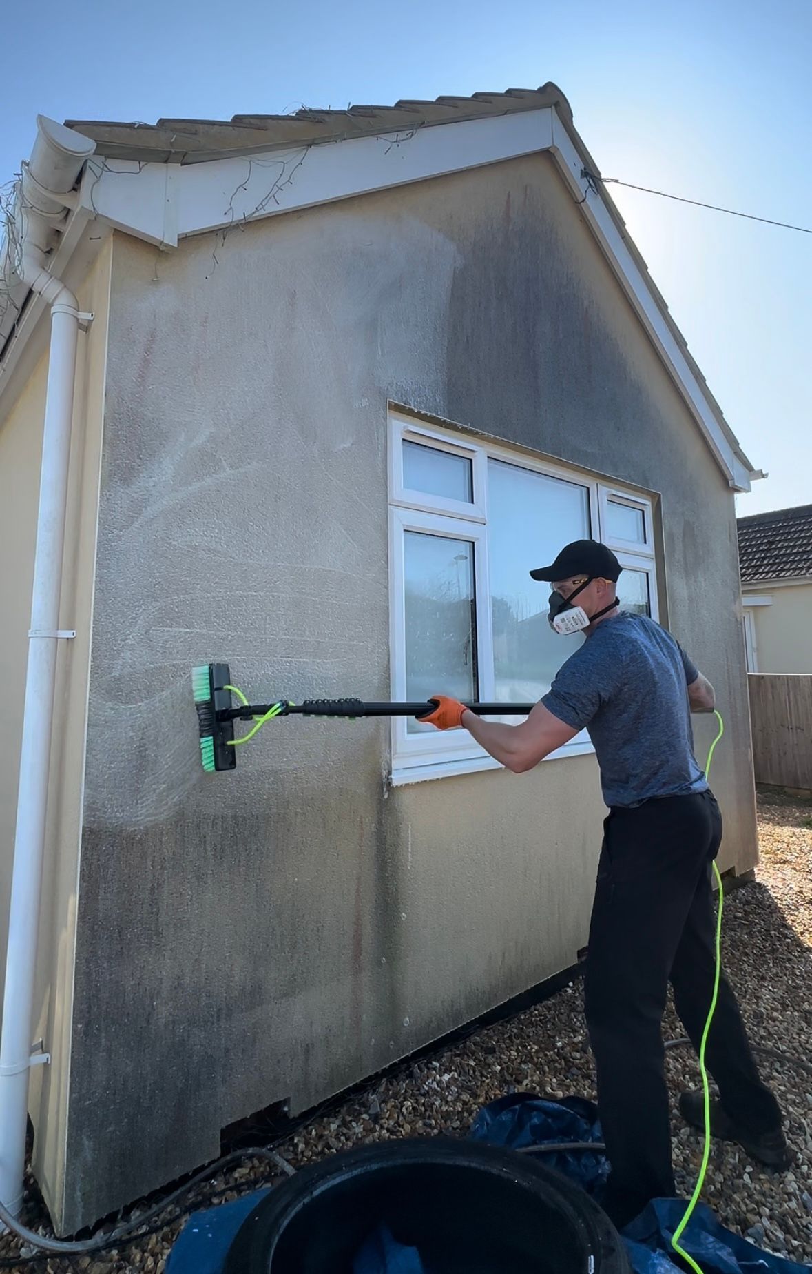A man is using a high pressure washer to clean a driveway next to a van.