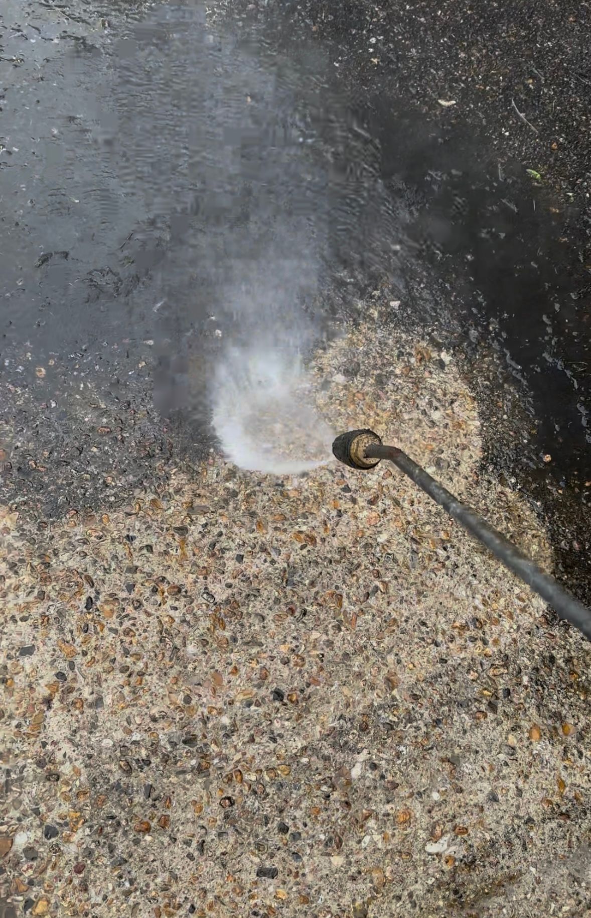 A man is using a high pressure washer to clean his driveway in front of his house.