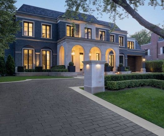 Beautiful circle driveway with dark paver stones and light concrete border with stone columns with lights