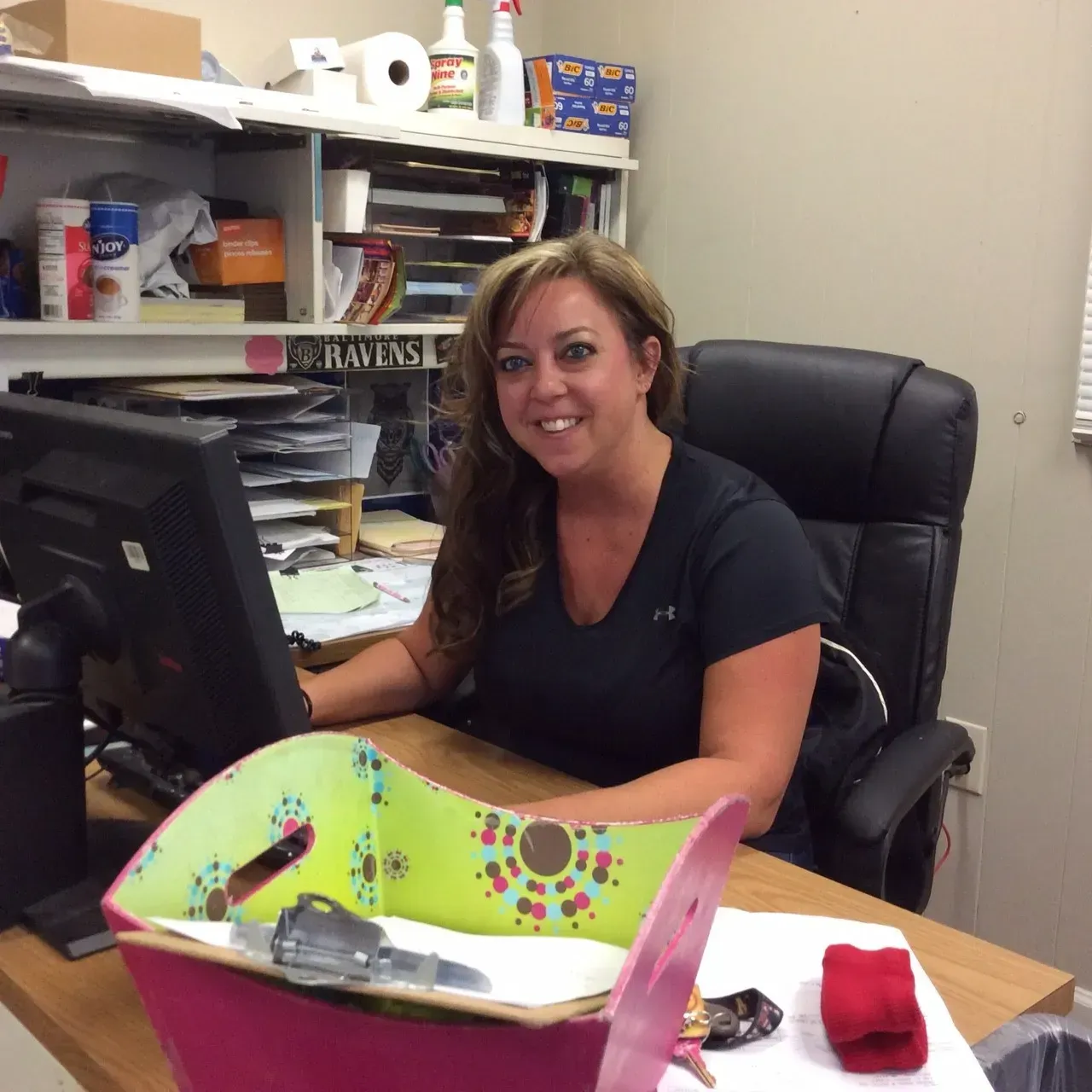 A woman sits at a desk in front of a computer with a sign behind her that says ' rams '