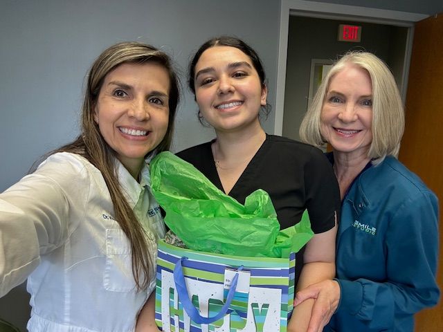 Three women are standing next to each other holding a gift bag.