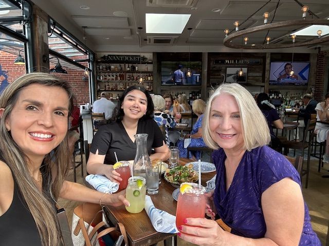 Three women are sitting at a table in a restaurant holding drinks.