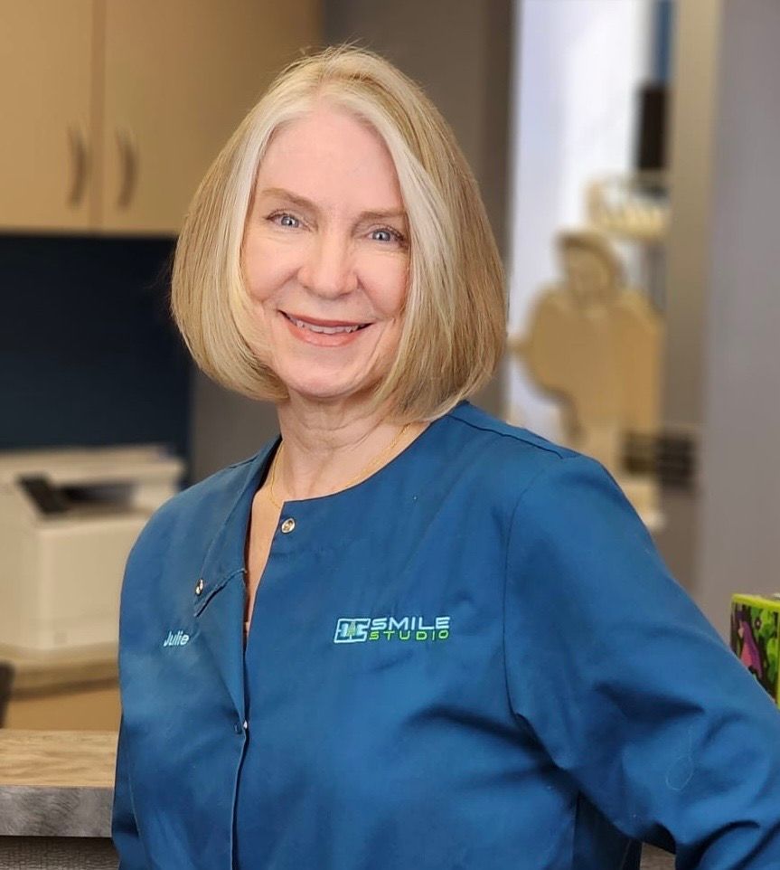 A woman in a blue jacket is smiling in a dental office.