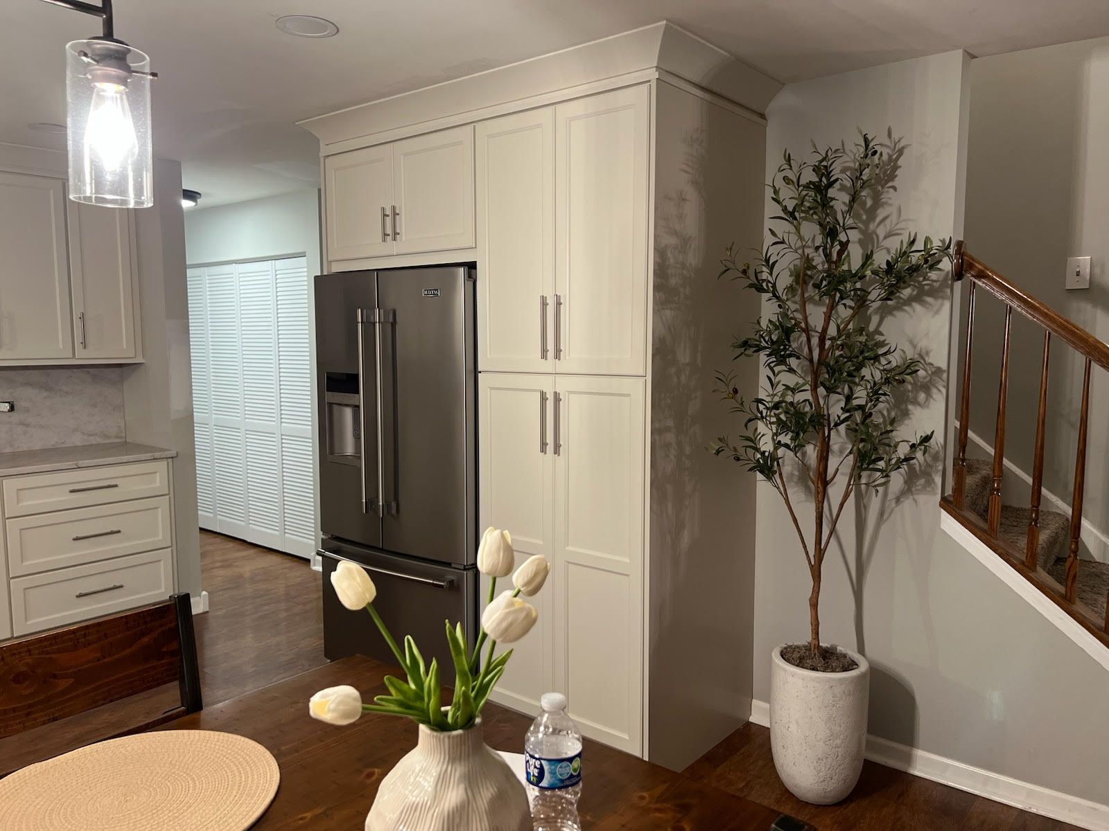 Kitchen with gray cabinets, refrigerator, and a tall plant. A vase of white tulips sits on the table.
