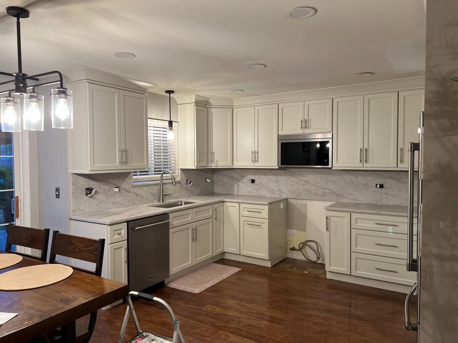 Kitchen with white cabinets, stainless appliances, marble backsplash, and dark wood floors.