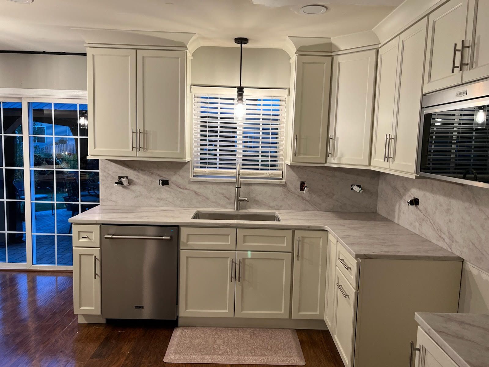 Beige kitchen with stainless steel appliances, marble countertops, and a window overlooking a backyard.