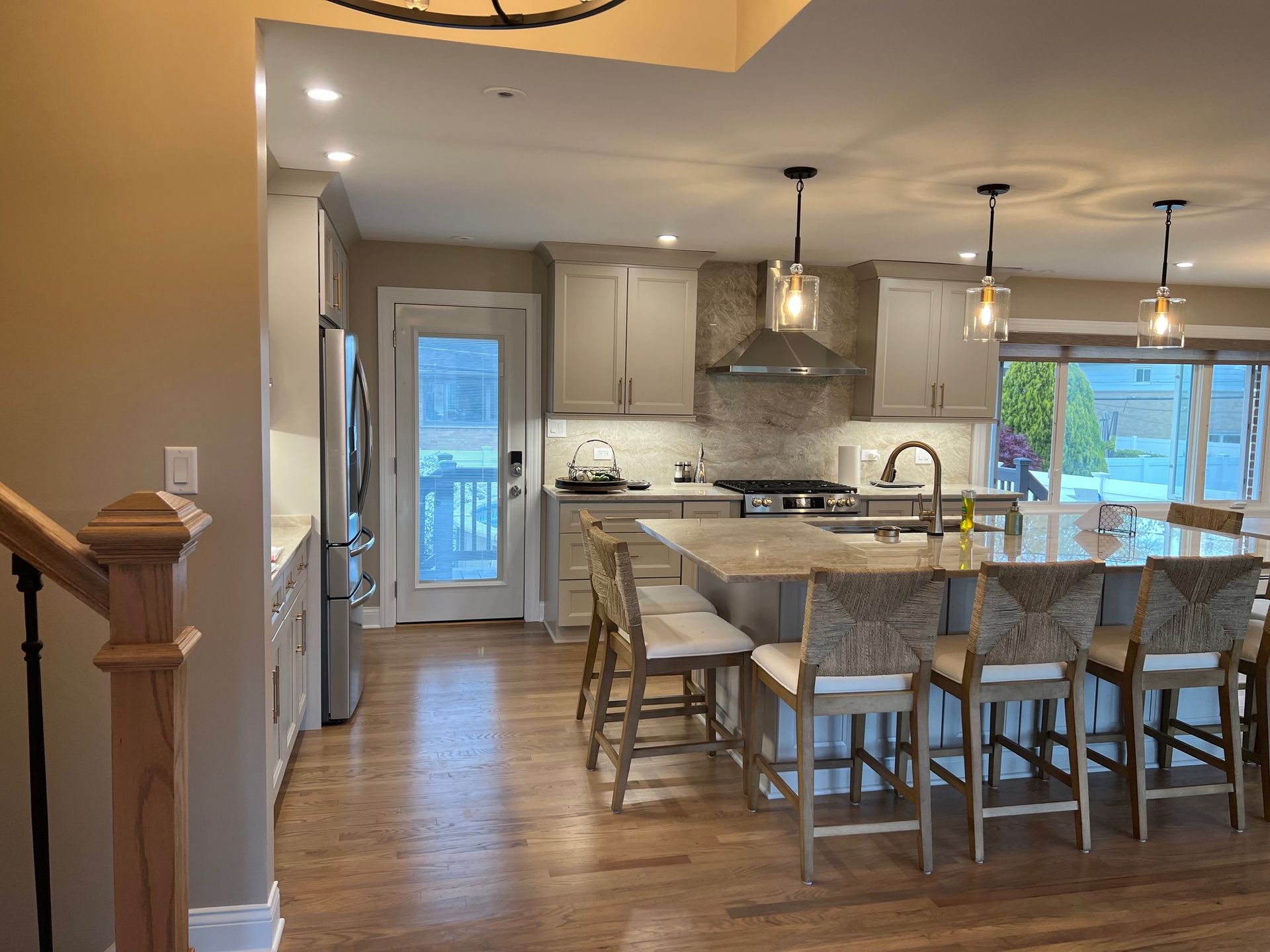 A kitchen with a large island, light cabinets, and bar stools.  Door to the backyard and stainless steel appliances.