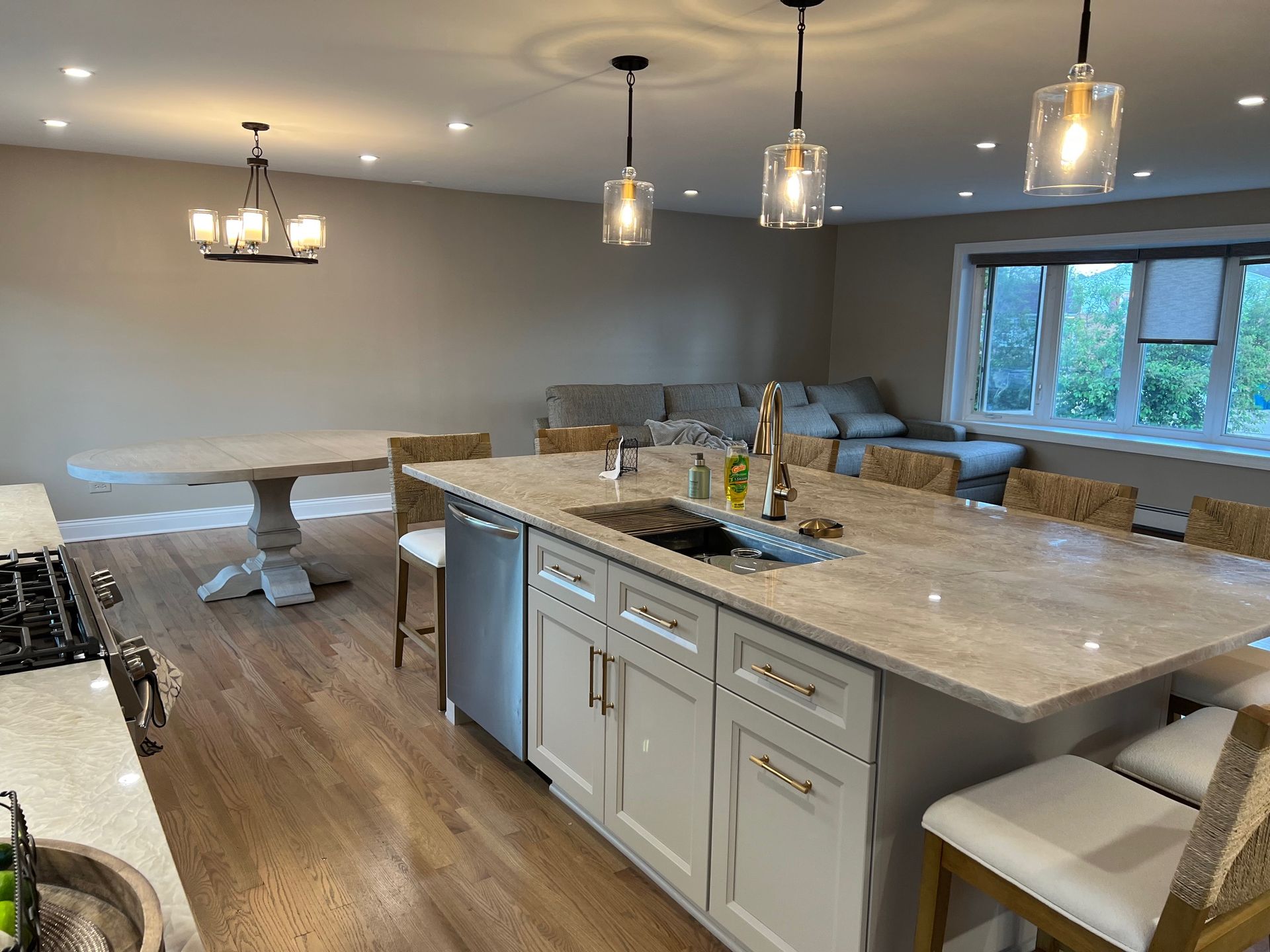 Modern kitchen with island, table, and seating. Light cabinets, granite countertops, and hardwood floors.