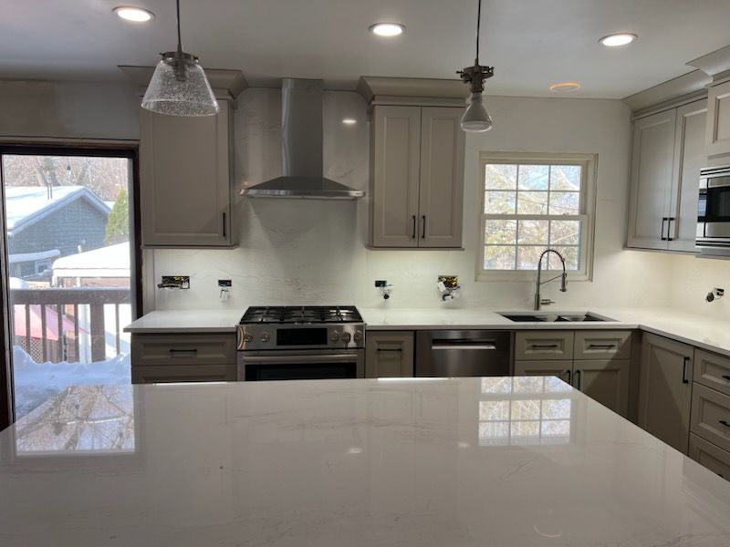 Modern kitchen with light gray cabinets, stainless steel appliances, and white countertops.