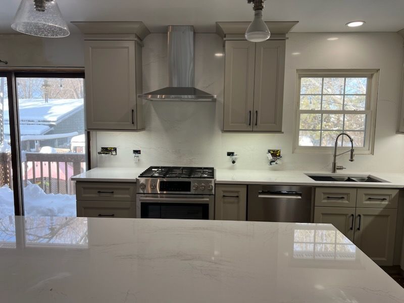 Modern kitchen with light cabinets, stainless steel appliances, and white countertops. View overlooks a snowy deck.