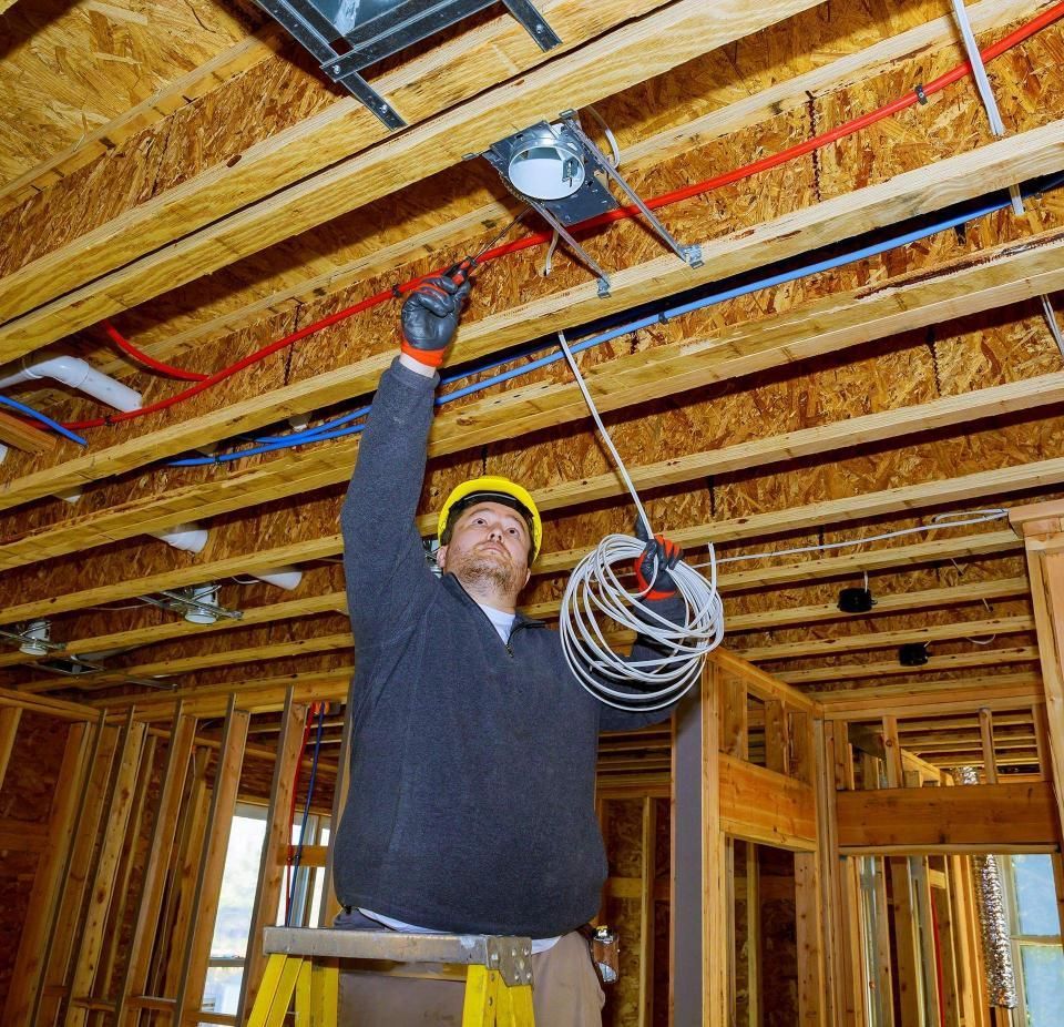 Electrician on a ladder installing wiring in a ceiling during construction.