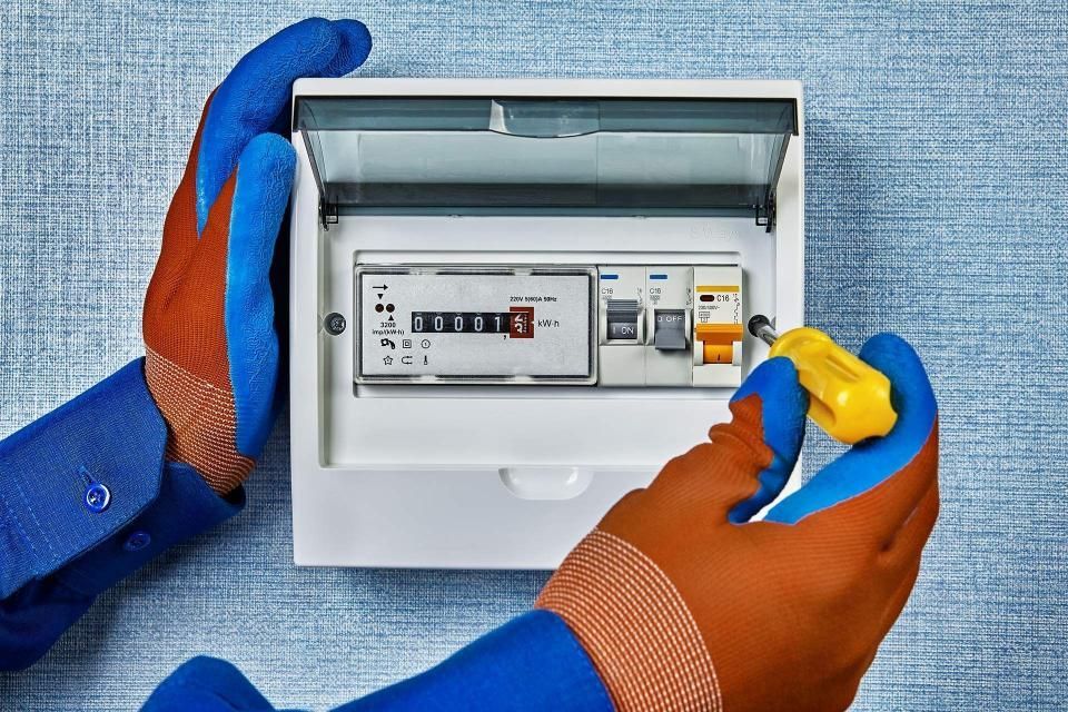 Hands in blue and orange gloves working on an electrical panel.