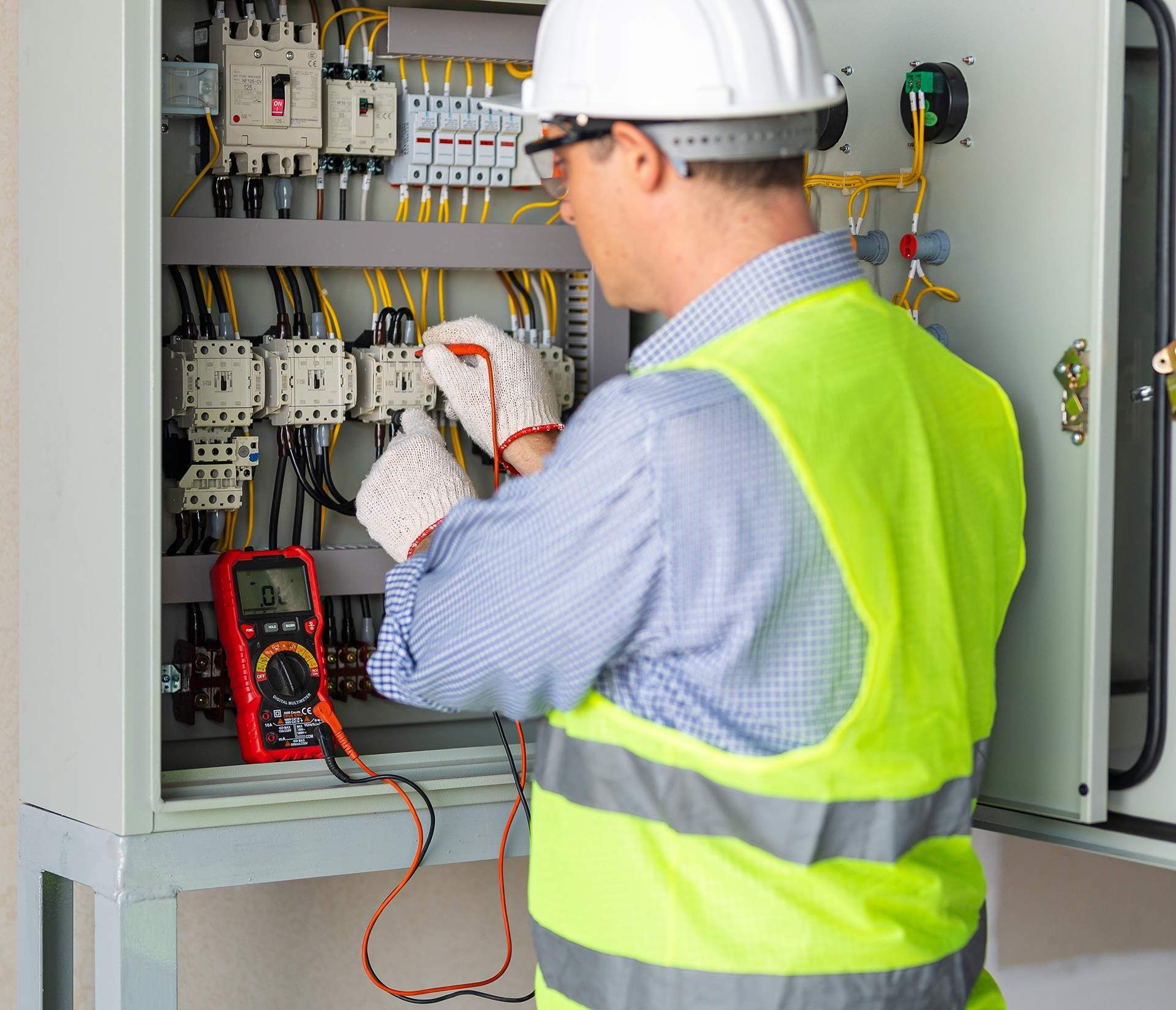 An electrician is working on an electrical box with a multimeter.