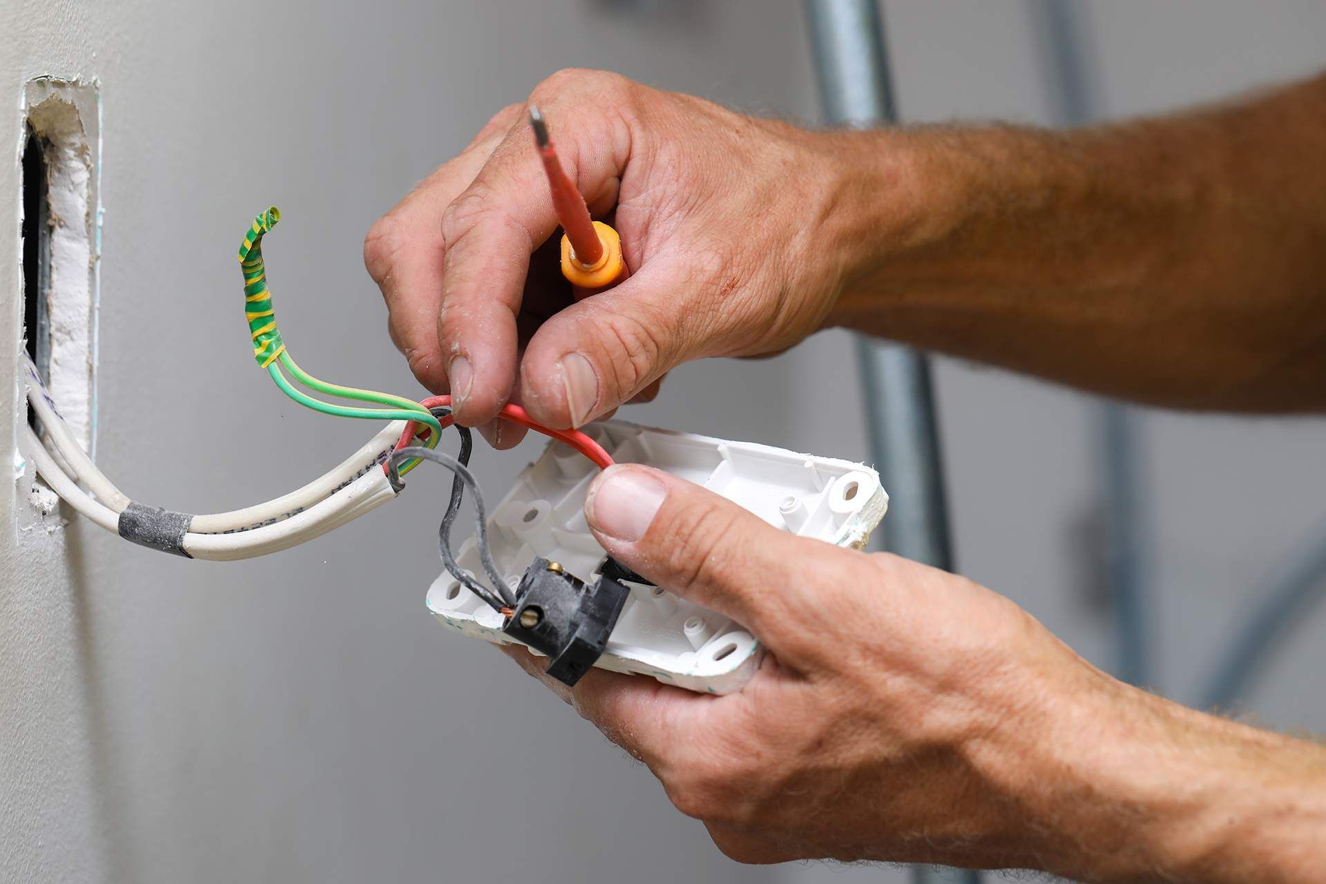Electrician connecting wires to a wall outlet; red and green wires, hands close up.