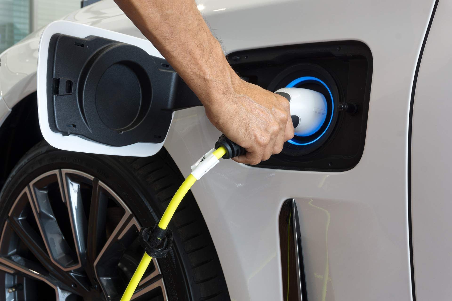 Hand plugging a yellow charging cable into an electric car's charging port on a white car.