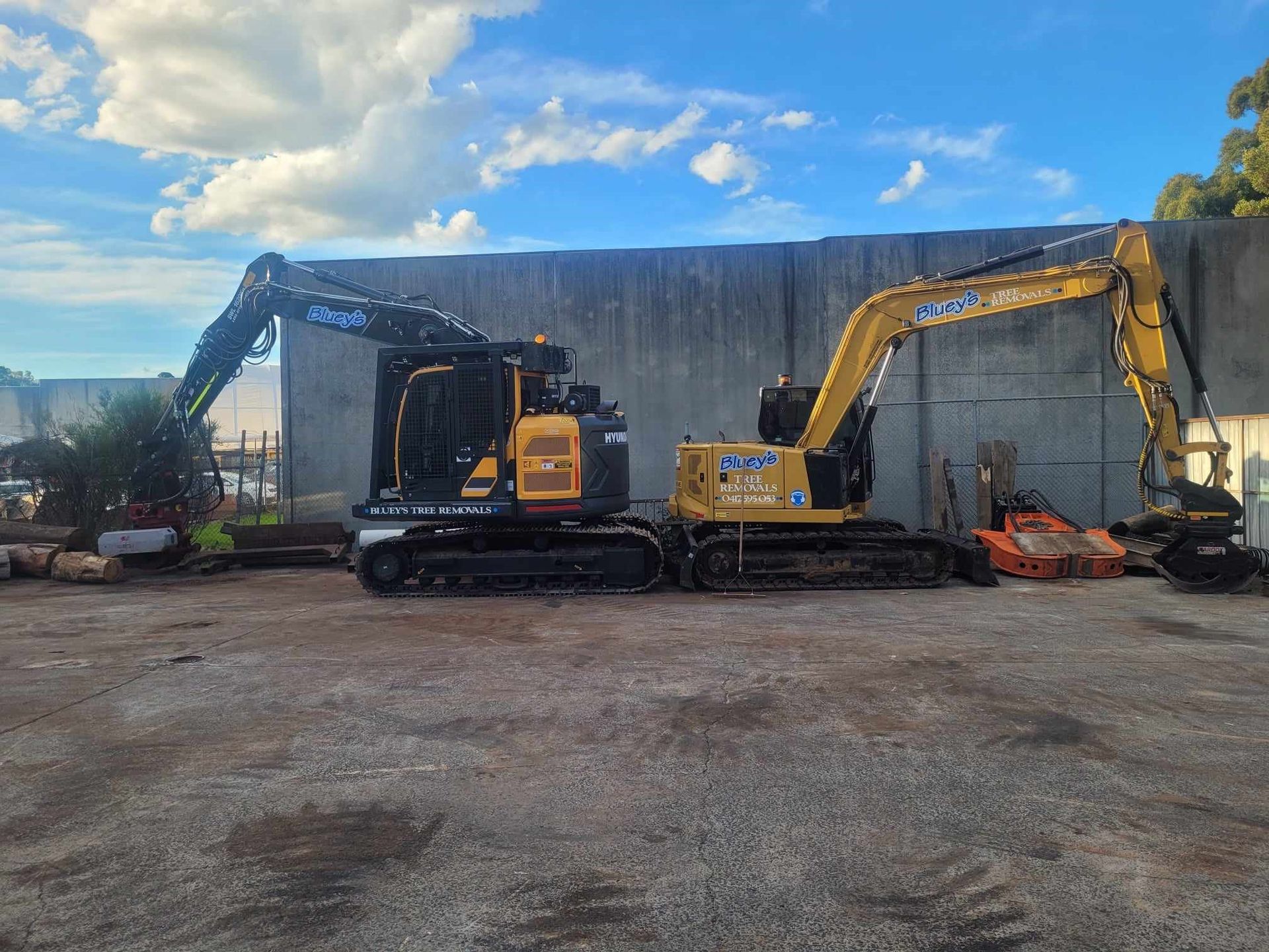 Two excavators are parked in a gravel lot in front of a building.