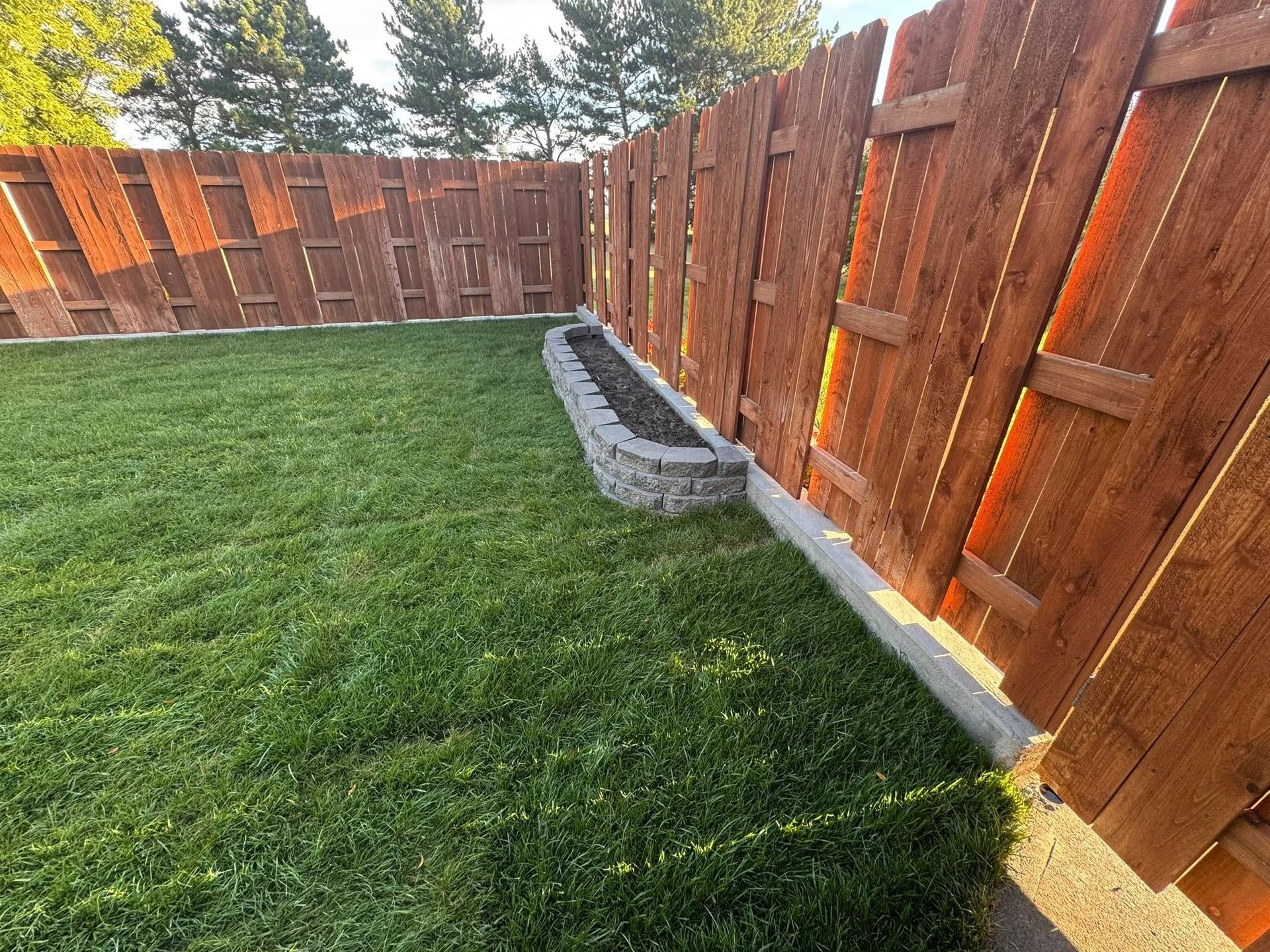 Backyard with green lawn, wooden fence, and raised stone planter along the fence line