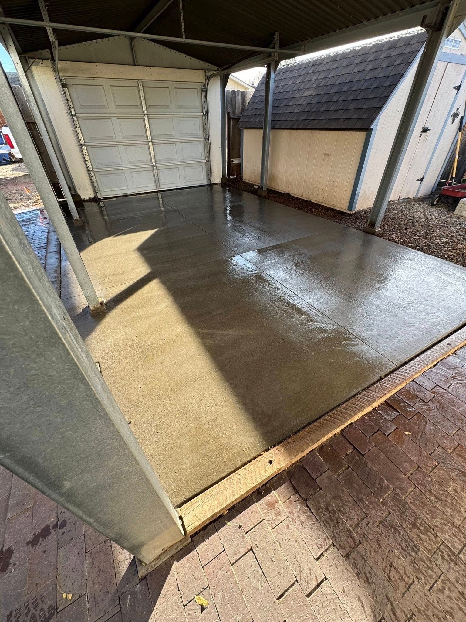 Wet concrete floor in a covered garage or carport, with white storage doors and wall panels.