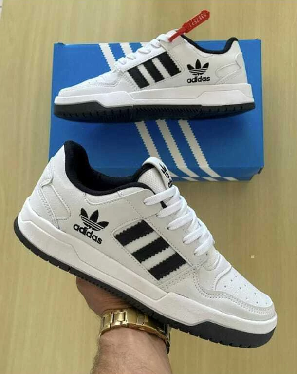 Zapatillas Adidas blancas con rayas negras y logotipo, sobre una caja de rayas azules y blancas, sostenidas por una mano.