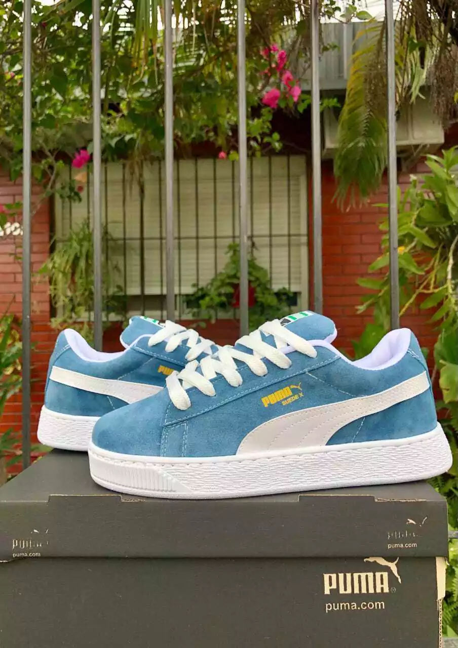 Zapatillas Puma de gamuza azul con detalles y cordones en blanco, apoyadas sobre una caja de zapatos.