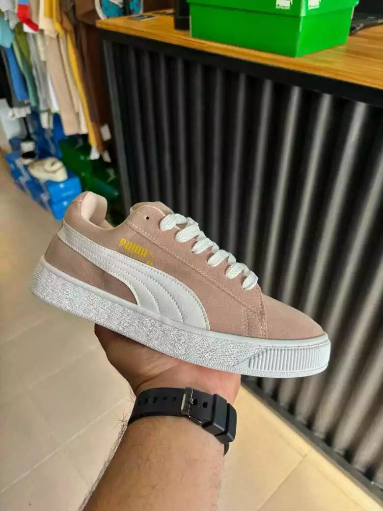 Persona sosteniendo una zapatilla Puma rosa con suela y logotipo blancos, en una tienda.