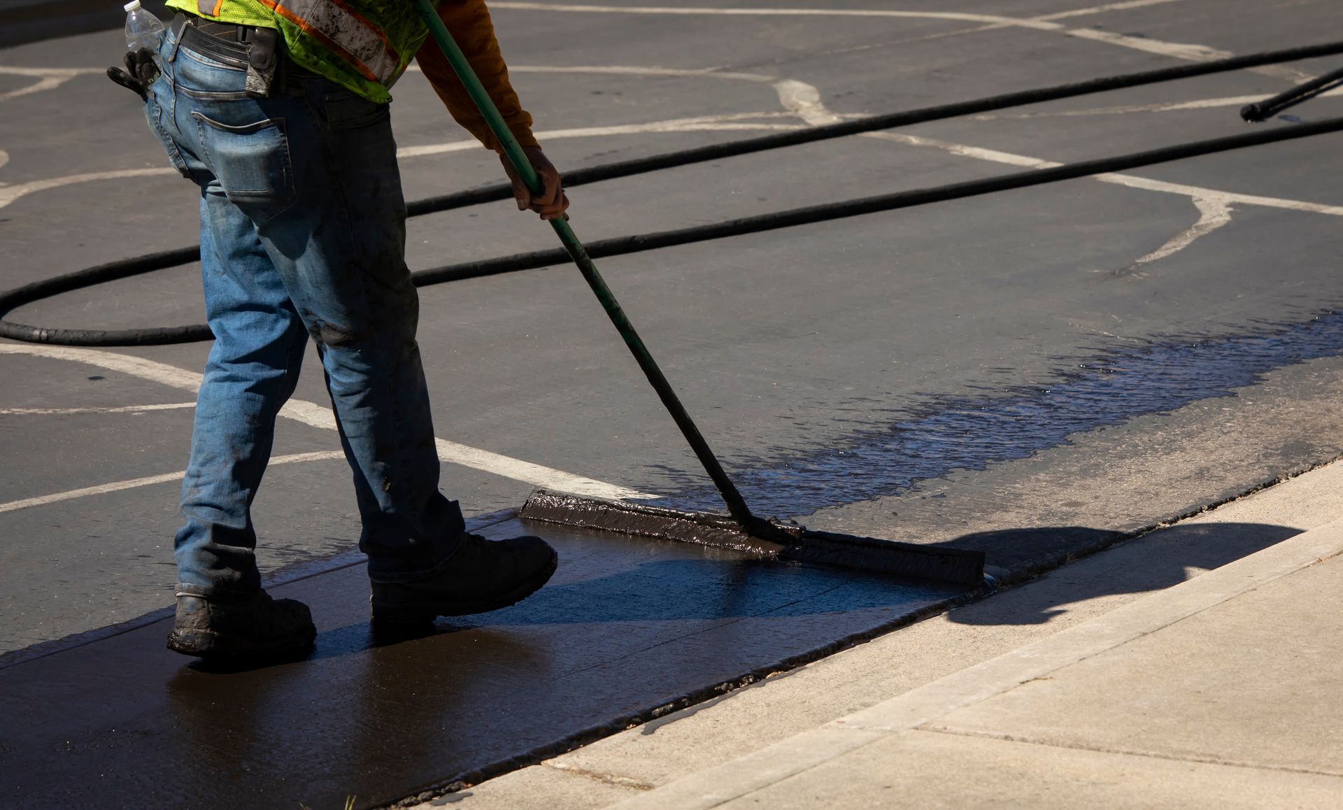 An industrious worker expertly applies a fresh coat of asphalt sealcoating with precision and care, ensuring a smooth and durable surface.