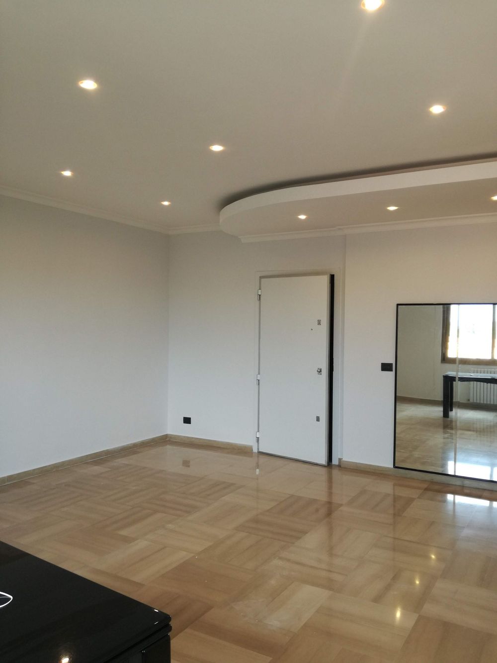 Stanza moderna vuota con pavimento in legno lucido, pareti bianche, faretti a incasso sul soffitto e anta dell'armadio a specchio.
