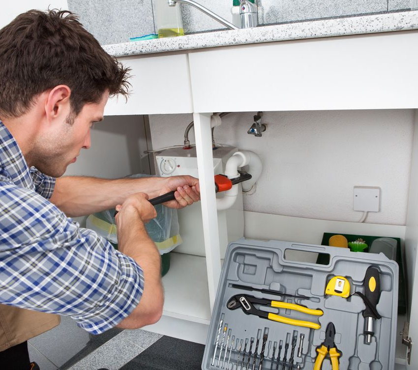Man, Repairs Pipes Under a Sink with a Wrench— Zac Rennick Plumbing in Dubbo, NSW