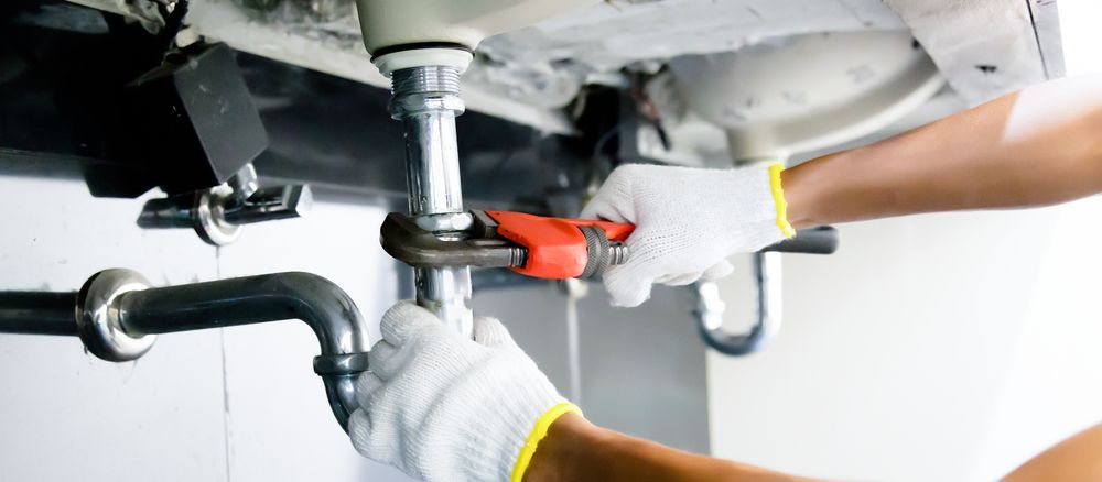 A Person Using a Wrench to Repair Plumbing Under a Sink — Zac Rennick Plumbing in Wellington, NSW