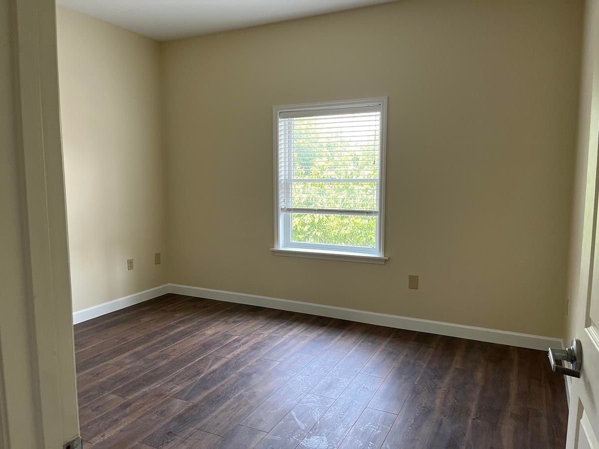 An empty bedroom with hardwood floors and a window.